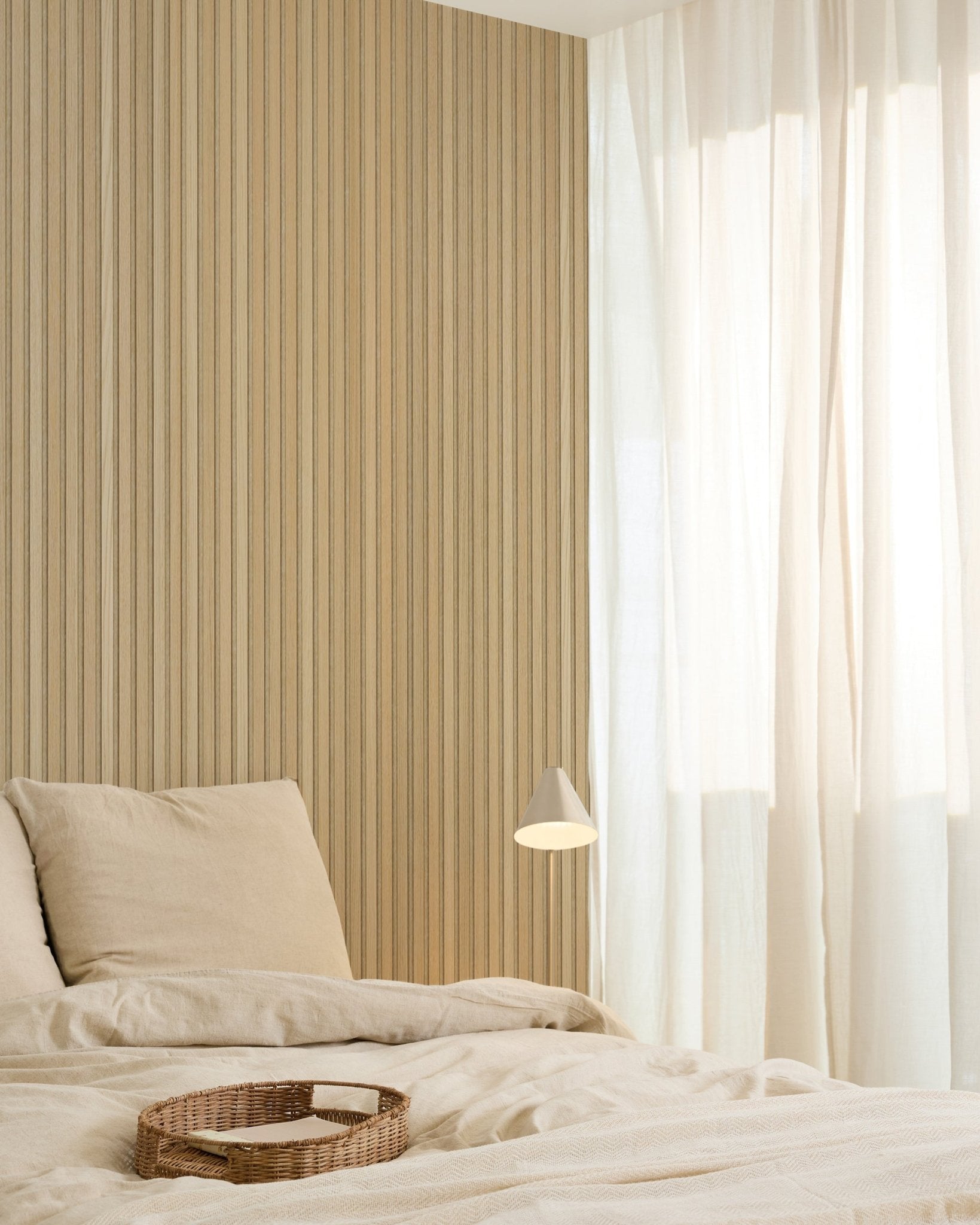 Camera da letto minimalista con biancheria da letto beige, un vassoio in vimini, una moderna lampada da parete, una parete d’accento in pannelli acustici di legno Akupanel e tende velate che diffondono una morbida luce naturale.